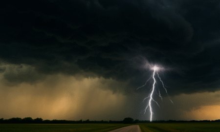 A dramatic landscape showing a severe thunderstorm with dark, heavy clouds and a bright lightning strike touching down over an open rural field.